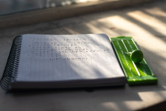 Stock photo of embossed Braille notebook next to green writing slate and stylus in natural light