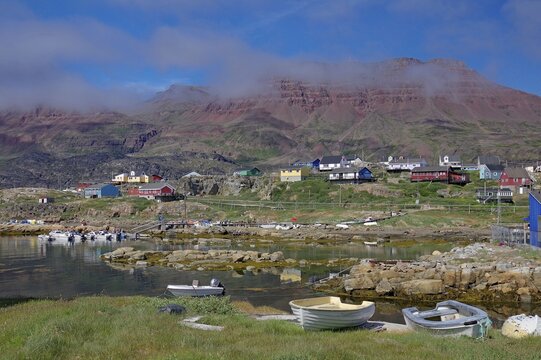 Small boats lie in front of houses and red volcanic mountains, dissipating fog, Qeqertarsuaq, Disko Island, Qeqertarsuaq, Arctic, Greenland, Denmark