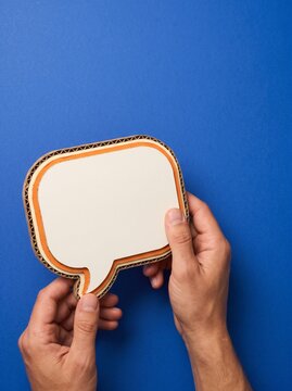 This captivating image showcases a pair of hands delicately holding a blank speech bubble against a vibrant solid royal blue background offering a space for