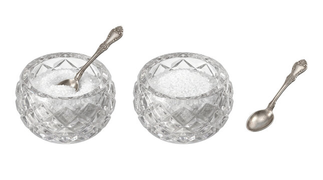 Two cut glass bowls filled with white granulated sugar and one ornate silver teaspoon on a white surface isolated on a transparent background