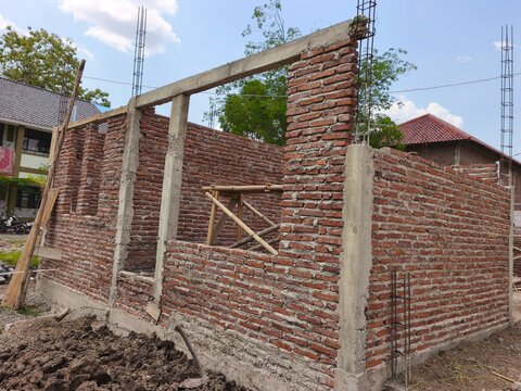 Unfinished residential building construction site featuring red brick walls, concrete beams, and steel rebar, ideal for civil engineering, house development, and architecture stock photo.