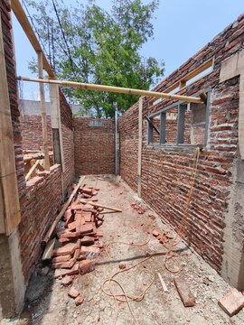 Unfinished residential building construction site featuring red brick walls, pile of bricks, window frames, and structural columns, ideal for civil engineering and house development stock photo.