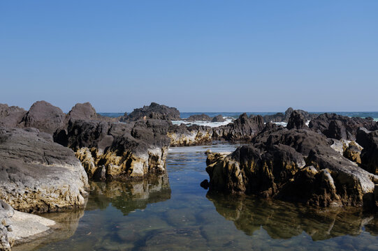 Calm tide pool reflecting volcanic rocks on a rocky coast in Japan