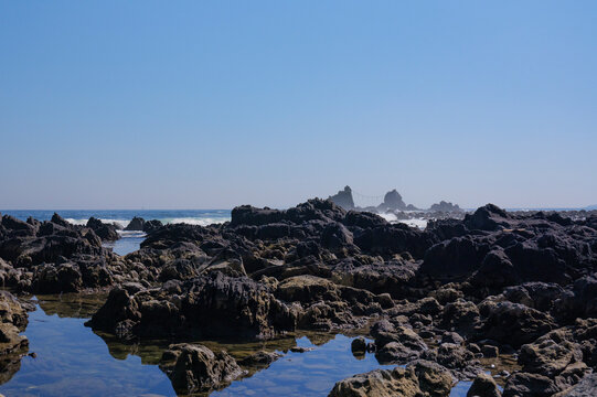 Tide pool and rugged lava rocks with distant Mitsuishi sea stacks