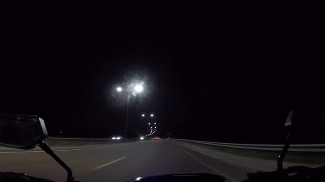 Forward view riding motorcycle on dark empty highway illuminated by bright street lights during midnight journey
