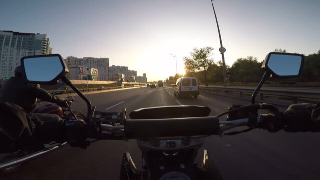 Forward view riding motorcycle along busy urban street with traffic under bright golden hour sunset