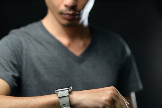 Young Man in Casual T-Shirt Looking at Smartwatch on Wrist Against Dark Background