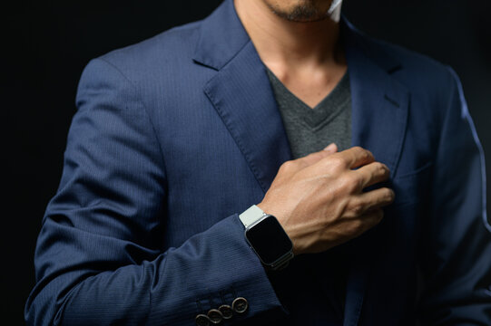 Man in Formal Blue Suit Wearing Smartwatch Gesture on Chest Against Dark Background