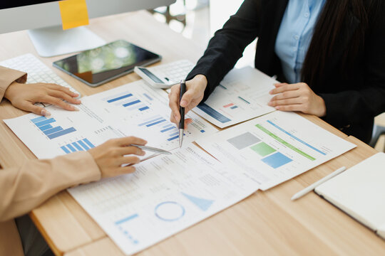 Office coworkers pointing to printed graphs and marking figures, comparing performance metrics and collaborating on financial reports during a business planning session
