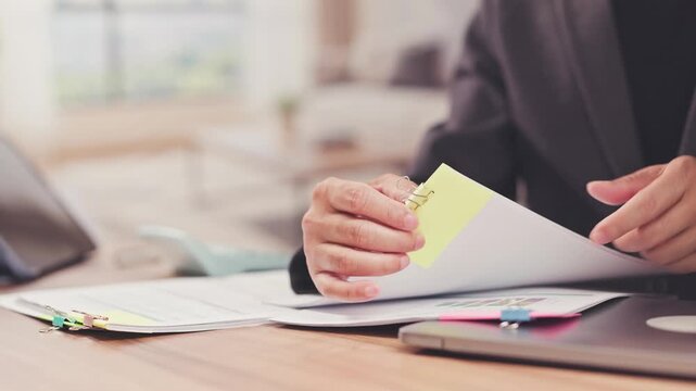 Businessman reviews paper report folders on office desk beside laptop. Corporate financial audit inspection, investment analytics research, annual accounting paperwork review.