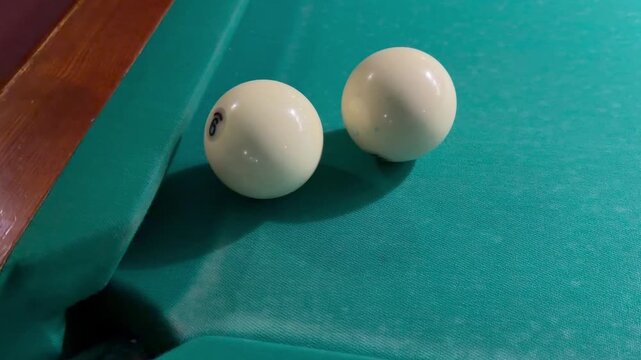 Two white Russian billiard balls sit near corner pocket on green felt table cloth. Sports game tournament equipment, leisure cue sport hobby activity, wooden pool table frame, active recreation match.