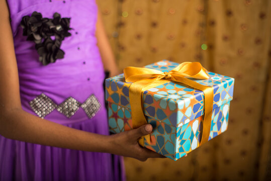 A young girl receving a beautiful gift box. Partial view of an arm holding gift pack. Festive gifts and celebration photos.
