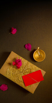 Diwali festive celebration gifts photo with blank tag for message. A golden gift box placed with Diwali lamp and flowers. View from above.