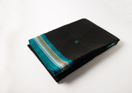 Neatly folded black color saaree with blue color border on white backround. Traditional Indian women ware- Saari, a 7 yard long fabric which is draped around.
