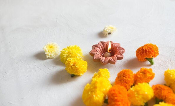 Earthen Diwali lamp placed with many fresh marigold flowers on white background. Indian festive background for auspicious and religious occasions.