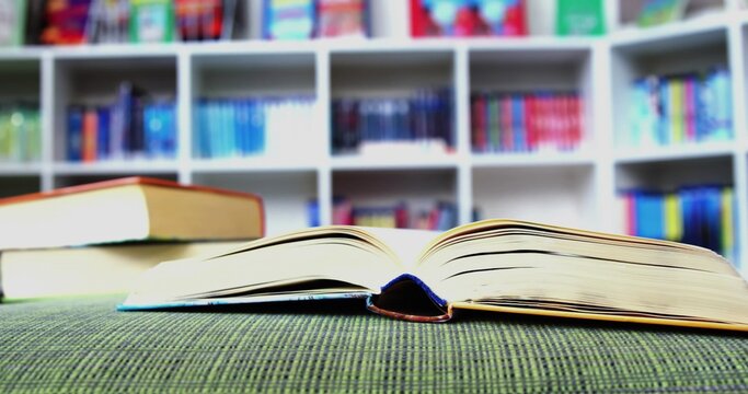 Showing open hardback book lying on green fabric in library, with stacked books left