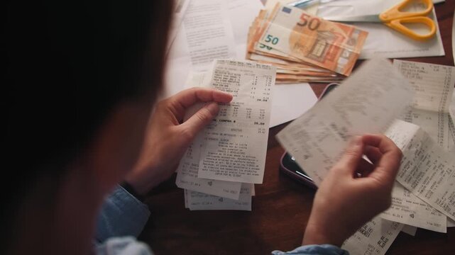 A woman calculates monthly expenses, for a period going through her purchase receipts and adding up on a calculator. Concept of a family budget. High quality 4k footage