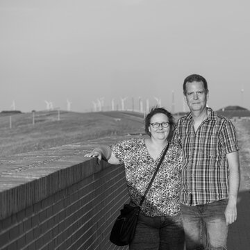Couple posing beside a brick wall with wind turbines in the countryside