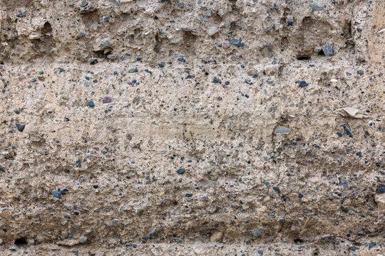 Detailed close-up captures rough texture of clay wall. Small stones and pebbles of various colors are embedded, showcasing natural imperfections and irregularities.