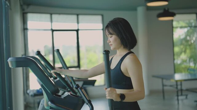 Young woman exercising on elliptical machine in bright modern gym with large windows and natural light