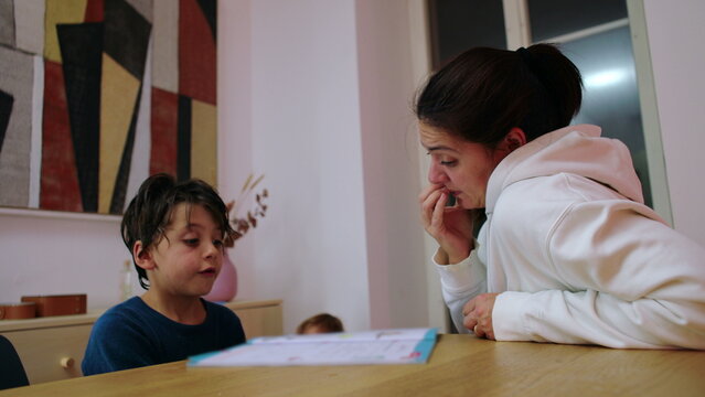 Homeschooling mother listens to her child review a lesson at the family table during nighttime study, fostering concentration, confidence and authentic home learning