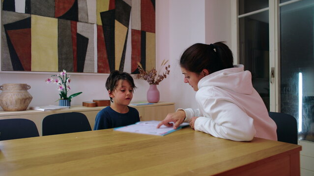 Mother supervises her child completing home study at the dining table at night, promoting independent learning, steady attention and responsible educational habits