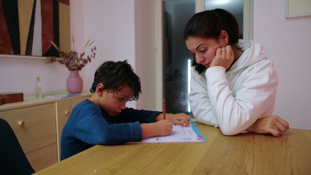 Mother supervises her child completing home study at the dining table at night, promoting independent learning, steady attention and responsible educational habits