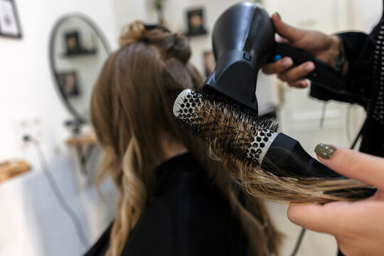 Hairstylist blow drying long brown hair with a round brush in a salon