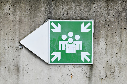 Emergency assembly point sign on concrete wall. Indicates designated safe meeting area for evacuation or disaster situations