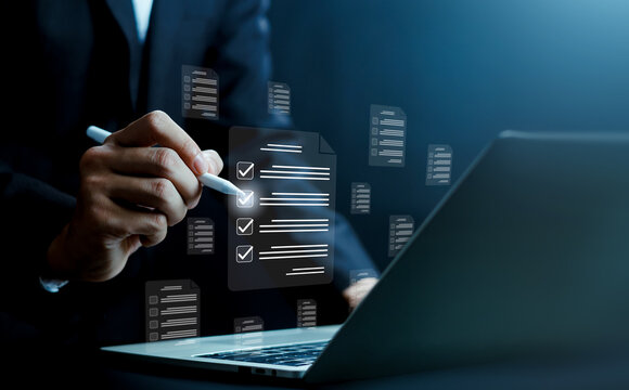 Business person using a stylus to check items on a digital checklist document interface over a laptop. Concept of task management, workflow tracking, project planning, and corporate productivity.