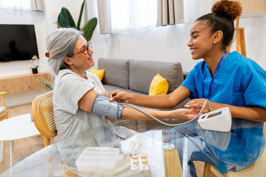 Latina nurse measuring an elderly woman's blood pressure during a home healthcare visit, providing compassionate patient care