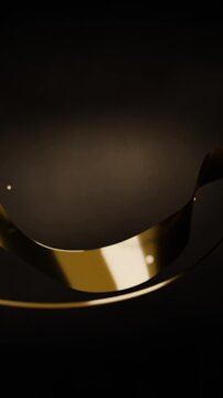 Vertical video: Appearing gliding gold ribbon revealing glossy sheen on dark backdrop