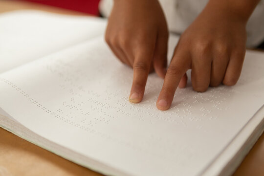 Hands reading braille text on page, fingers touching raised dots