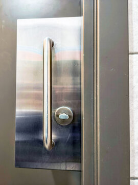 Modern metal door with long stainless steel pull handle and circular lock. Building entrance hardware. Access control and security concept. Contemporary commercial architecture