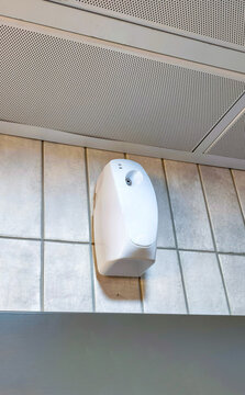 Automatic air freshener dispenser mounted on tiled public restroom wall. Hands-free fragrance dispenser for washroom hygiene. Sanitation and facility maintenance concept