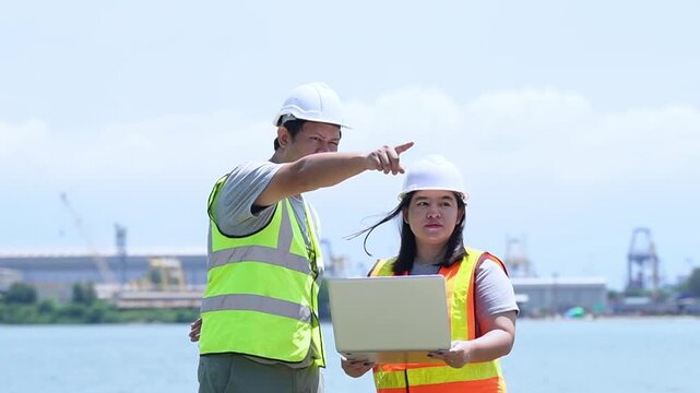 Industrial engineers discussing technical project data on laptop outdoors at construction site port
