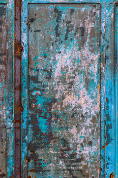 Close-up photograph of a weathered metal surface showcasing peeling teal and blue paint. Rust patches in brown and orange hues add to the distressed texture, creating an abstract composition.