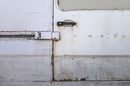 Detailed view of a white vehicle's side door, showcasing cracked and peeling paint. Rust is visible around the black door handle and seams, emphasizing age and wear.