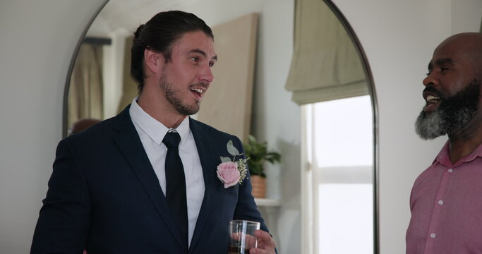 African American man in pink shirt hugging friend at wedding celebration indoors