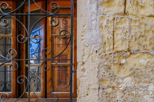 Black Wrought Iron Scroll Grille Over Wooden Framed Window Beside Rough Pitted Limestone Wall