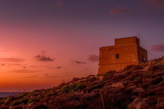 Stone Coastal Defense Watchtower Sitting on Hillside over Sea under Vibrant Pink and Orange Pastel Twilight Sky, Gozo Island, Malta