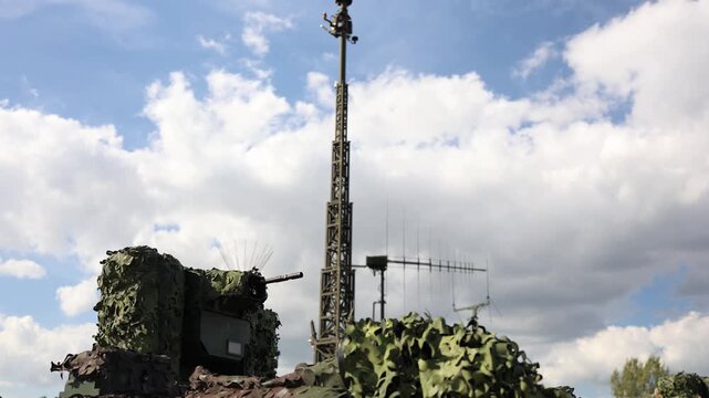 Camouflaged military air defense platform with an automatic cannon and elevated radar antenna mast designed for aerial threat detection surveillance and protection against hostile targets