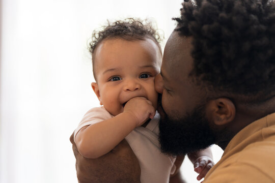 African American father kissing the cheek of newborn baby infant with kindly and love, adorable smiling mixed race baby, fatherhood moments, love and parenting care at home