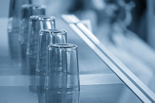 Row of plastic glasses on a conveyor belt after the injection molding process in a blue tone scene