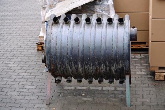 Heavy duty metallic convection wood burning stove with air tubes on paved tiles near pallets at warehouse. Burning stove, cylindrical horizontal combustion chamber made from bent solid steel pipes