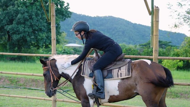 Woman riding brown and white horse outdoors in riding gear with helmet in natural green countryside landscape