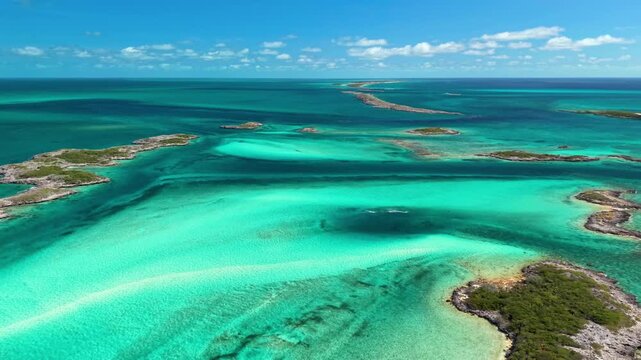 Allan Cay, Exuma, Bahamas: Aerial view of small rocky cays with green scrub and a tiny white hut above turquoise tidal flats, sandbars and clear shallow water under scattered clouds.