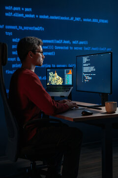 Developer is deeply focused on an AI and data science project, typing scripts across multiple screens in a dark workspace with running programming code on the background. Copy space. 