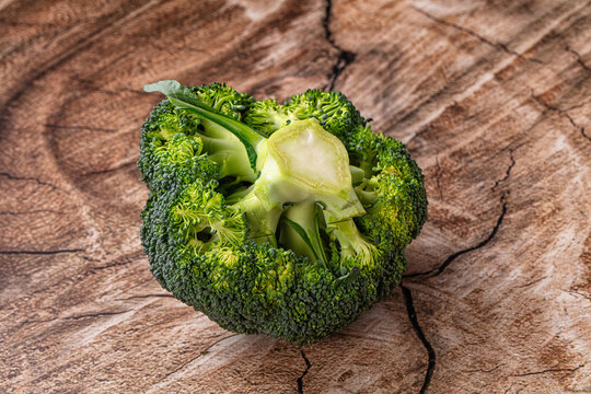 Fresh green broccoli head resting on rustic textured wooden surface, raw vegetable ingredient on wood table
