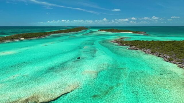 Ship Channel Cay, Exuma, Bahamas: Aerial view of turquoise tidal channel between green scrub-covered cays, with sandbars, rocky shores and white sand beaches under a blue sky with small clouds.